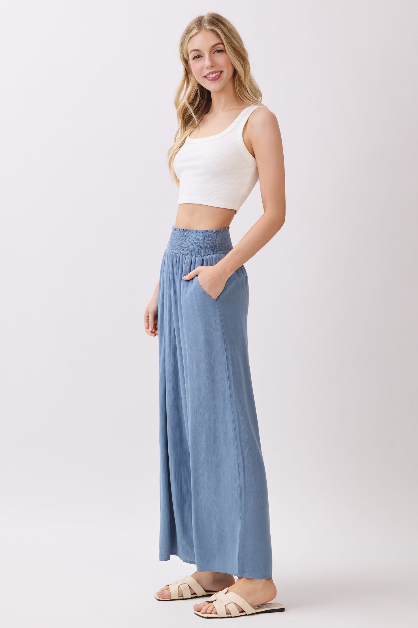 woman wearing a white cropped tank top and blue wide-leg pants with a smocked waistband, posing sideways