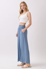 woman wearing a white cropped tank top and blue wide-leg pants with a smocked waistband, posing sideways