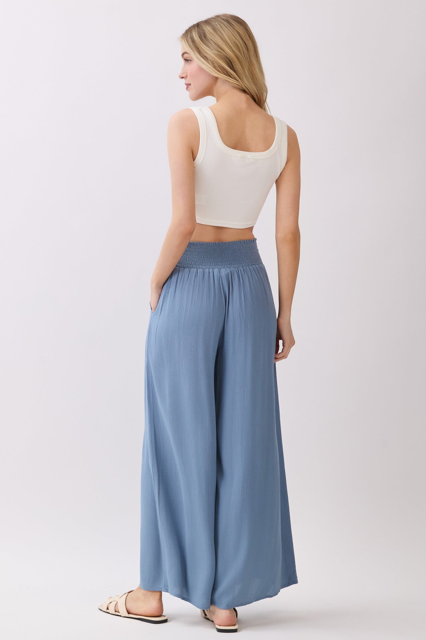 woman wearing a white cropped tank top and light blue wide-leg pants with an elastic waistband, standing with her back to the camera