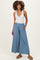 woman wearing a light blue maternity jumpsuit with wide legs and a smocked waistband, standing with hands in pockets