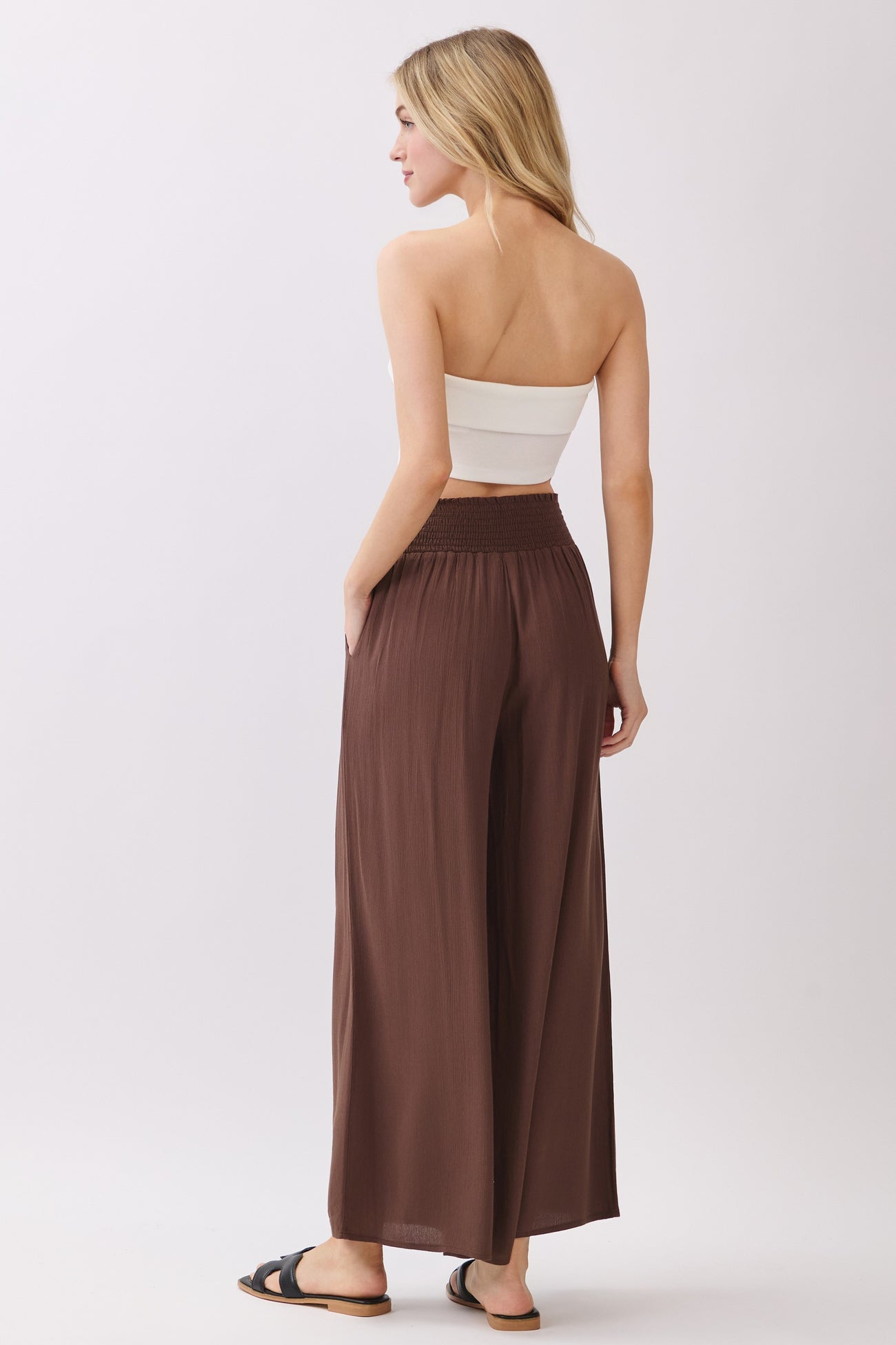 woman wearing a brown high-waisted wide-leg pant with a smocked waistband and a white cropped top
