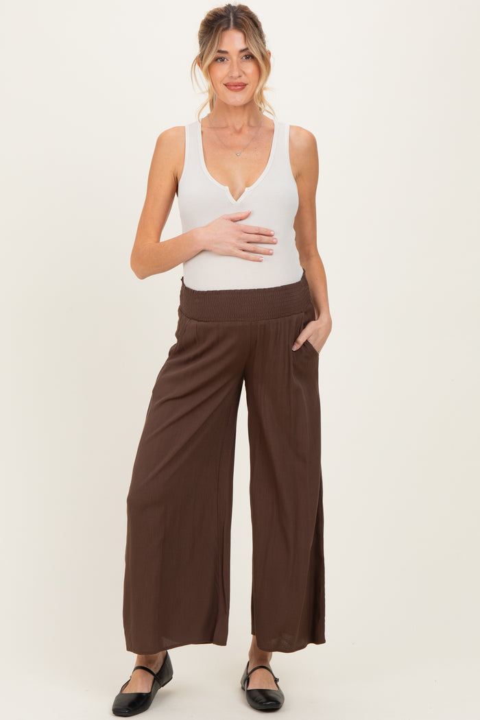 woman wearing a white fitted maternity tank top and brown wide-leg maternity pants, showing her baby bump