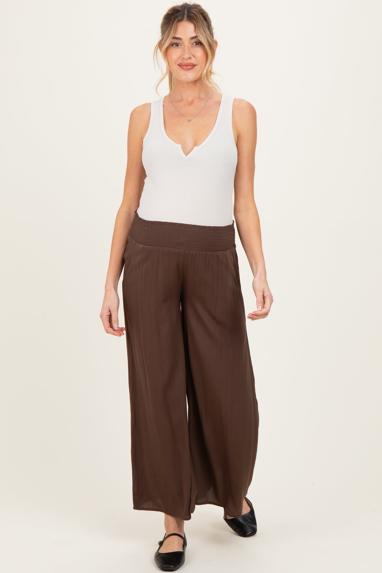 woman wearing a white sleeveless maternity top and brown wide-leg maternity pants
