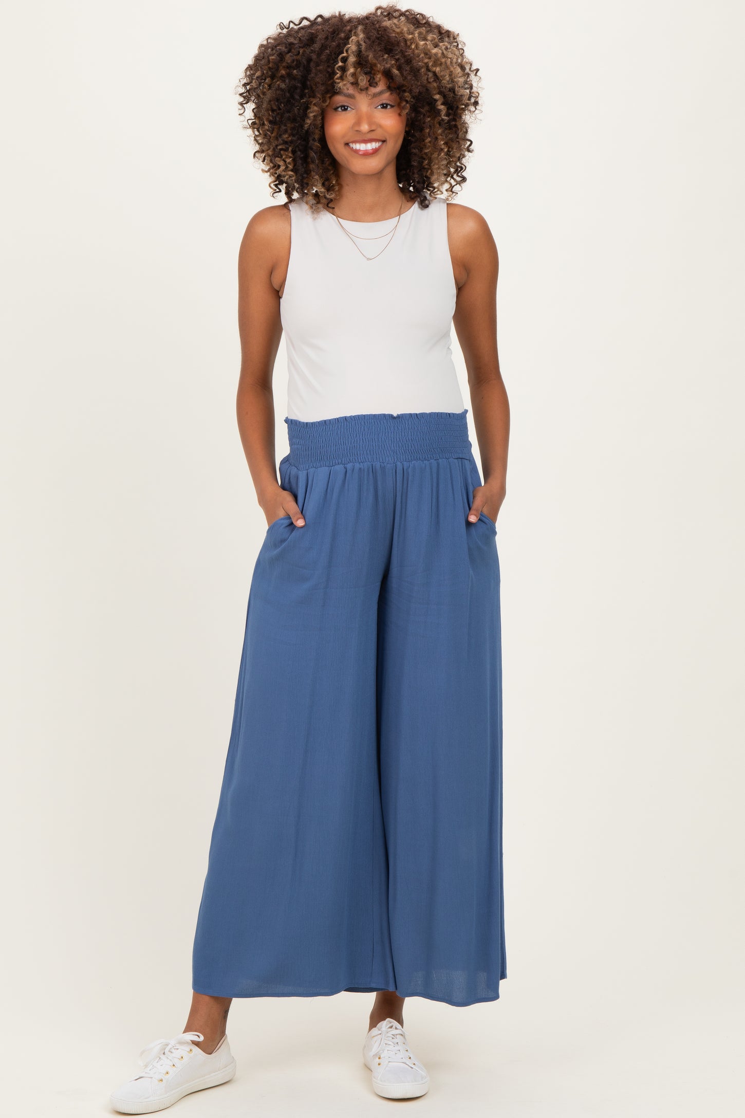woman wearing a gray sleeveless top and flowy blue maternity pants with a smocked waistband and side pockets