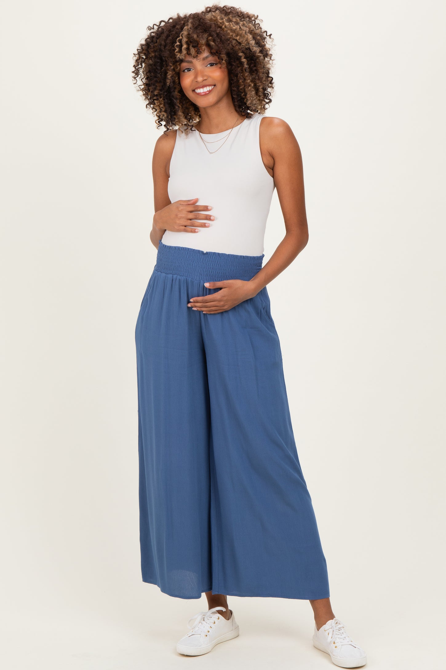 woman wearing a light blue maternity wide-leg pant and holding her baby bump