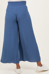 woman wearing blue maternity wide-leg pants, showing the back view with a smocked waistband and paired with white sneakers