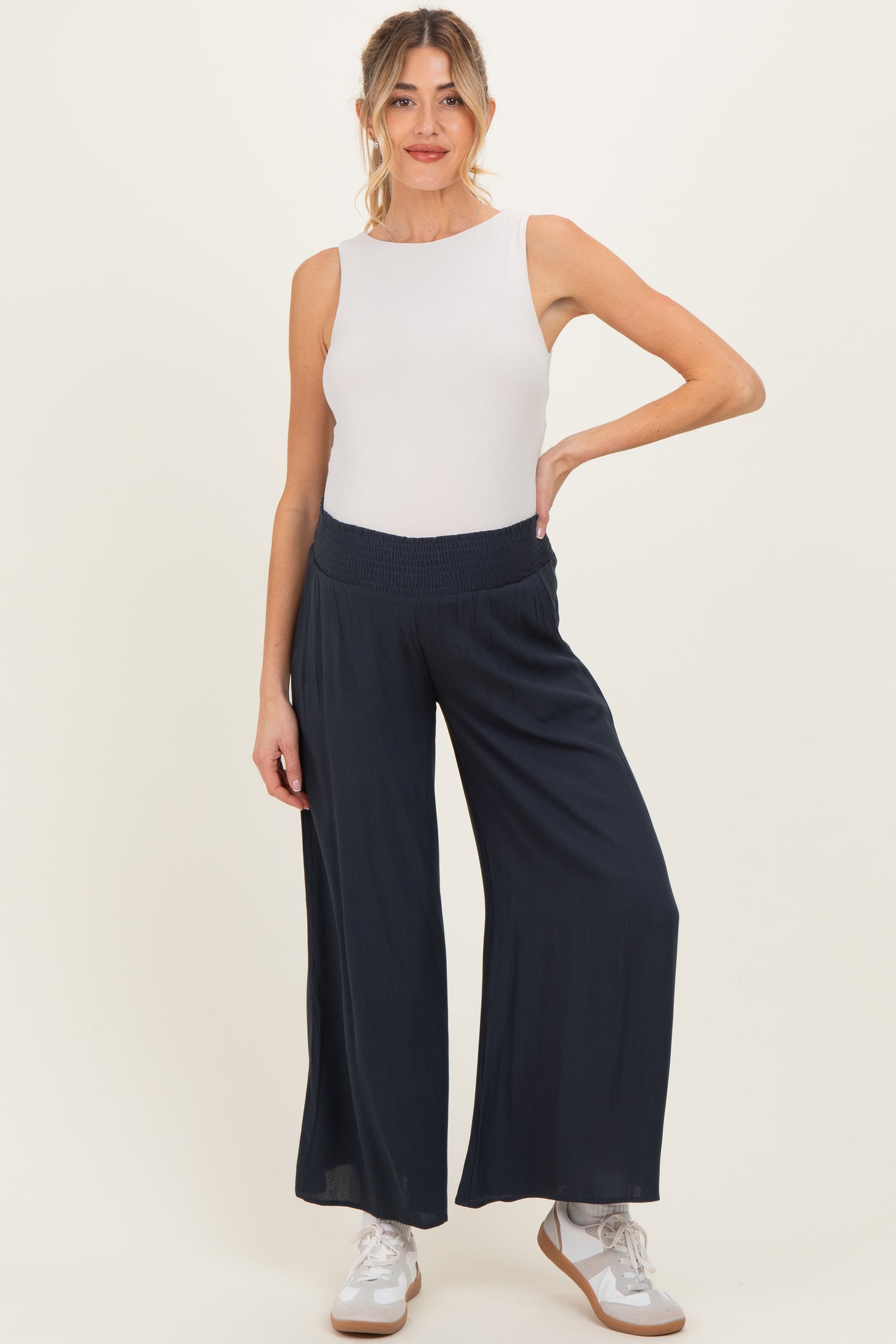 woman wearing a white sleeveless maternity top and navy wide-leg pants, with a relaxed fit and stretchy waistband