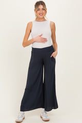 woman wearing a white maternity tank top and navy wide-leg maternity pants, holding her baby bump
