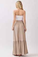 woman wearing a strapless white smocked top and a long beige tiered maxi skirt, viewed from the back
