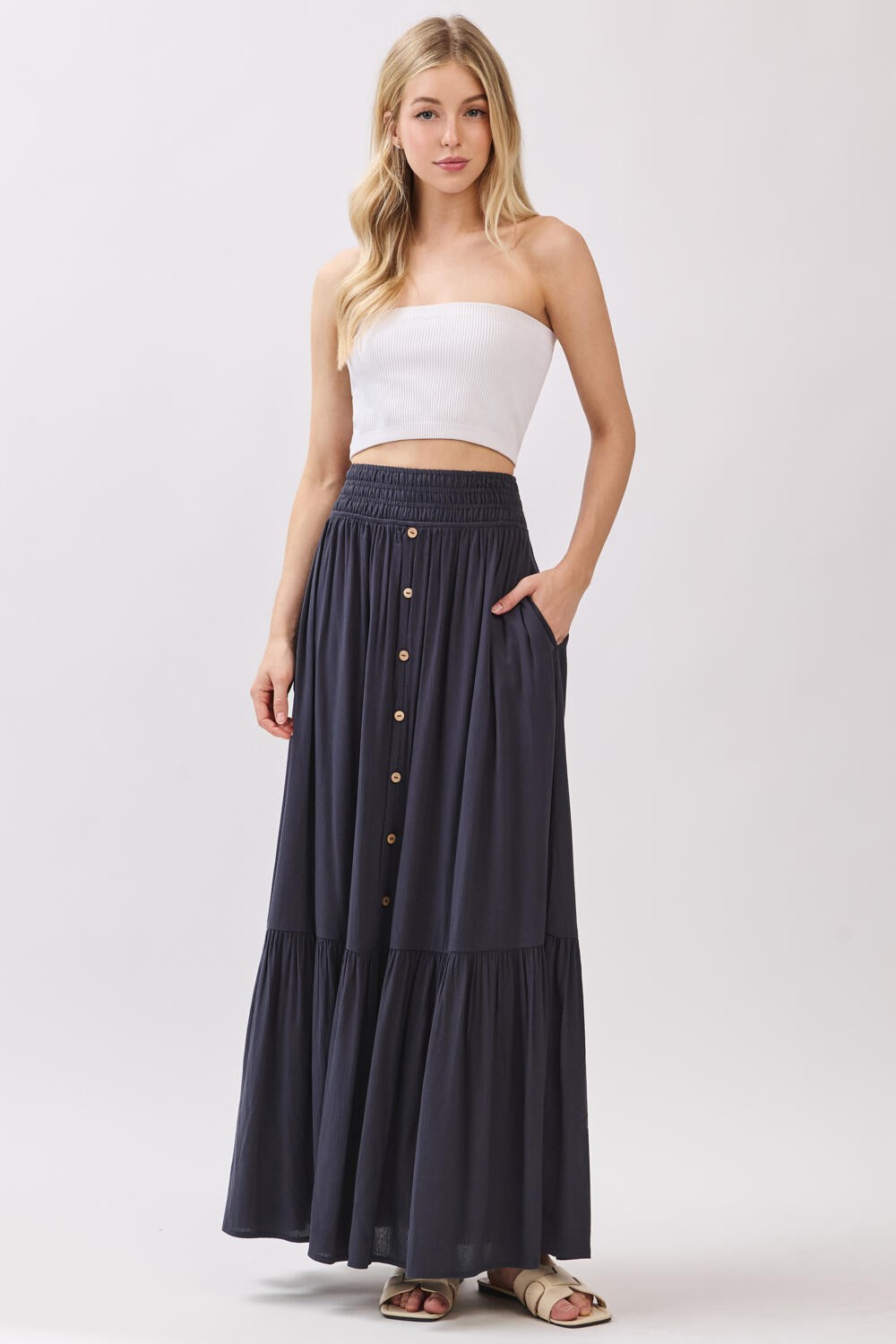 woman wearing a white strapless top and a navy blue maxi skirt with button details and pockets