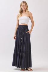 woman wearing a white strapless top and a navy blue maxi skirt with button details and pockets