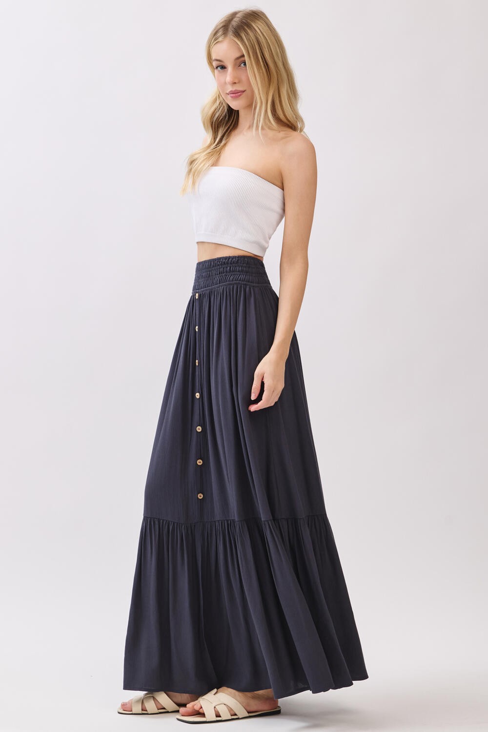 woman wearing a white strapless top and a navy blue maxi skirt with button details and a tiered hemline