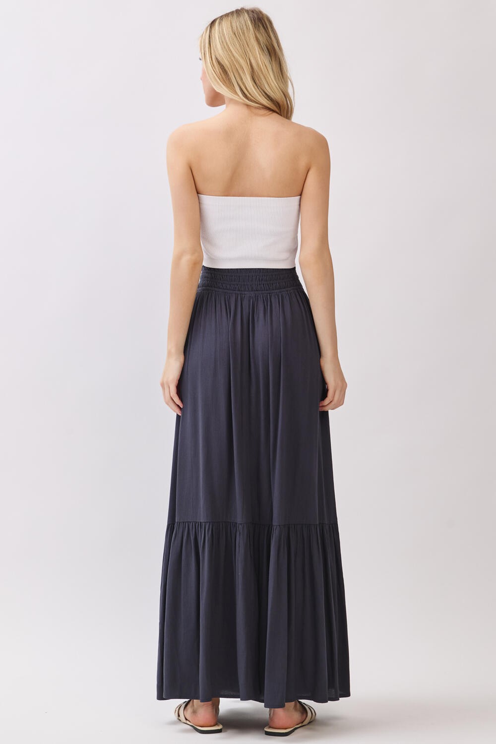 woman wearing a strapless white top and a long dark gray maxi skirt, view from the back
