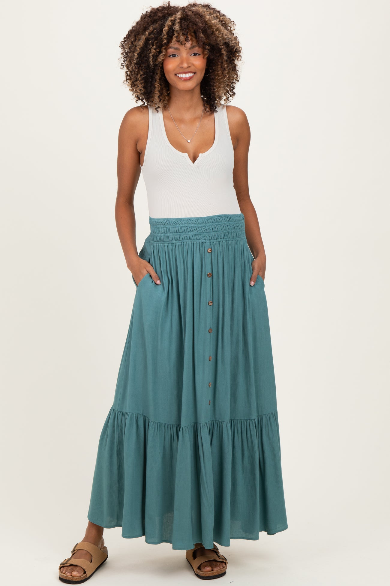 woman wearing a white tank top and a teal maternity maxi skirt with buttons and pockets