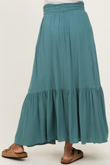 woman wearing a teal maternity maxi skirt with a tiered design and elastic waistband, standing with her back to the camera