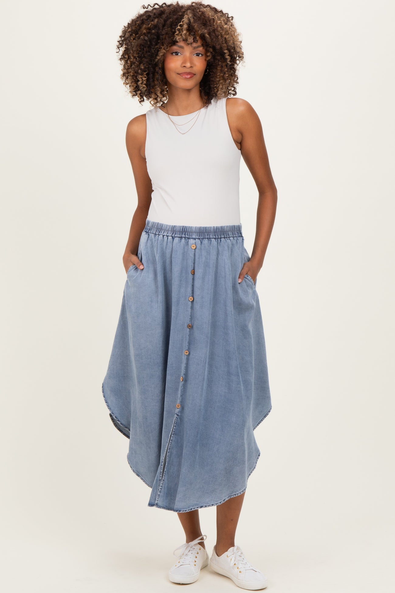 woman wearing a light blue denim maternity skirt with a button front and side pockets, styled with a sleeveless top