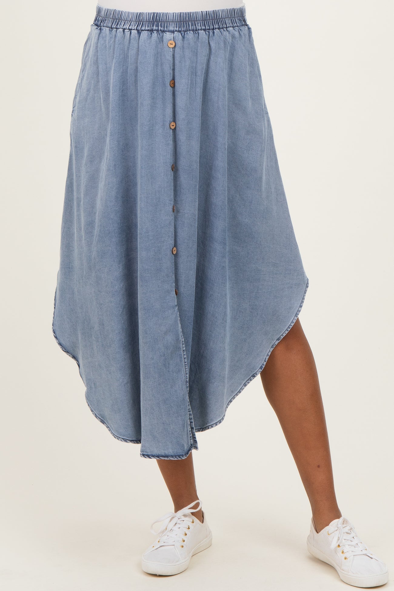 woman wearing a light blue maternity midi skirt with button detail and high-low hem, paired with white sneakers