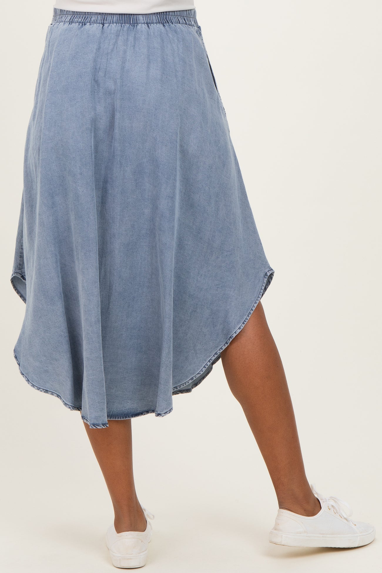maternity wear denim skirt in light blue with a flowy, asymmetrical hemline, modeled by a woman wearing white sneakers
