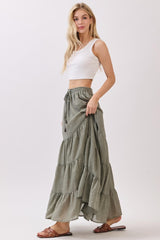 woman wearing a white crop top and a green tiered maxi skirt, standing with hands on her hips