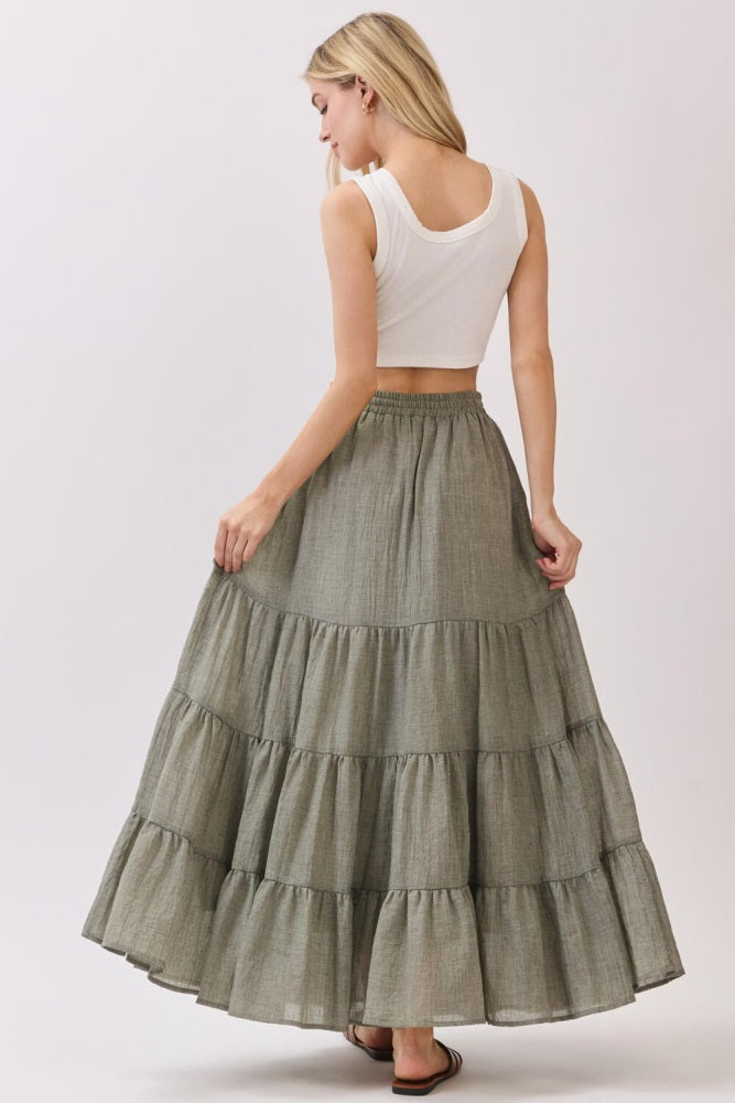woman wearing a white crop top and a long olive green tiered maxi skirt, seen from the back
