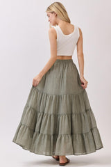 woman wearing a white crop top and a long olive green tiered maxi skirt, seen from the back