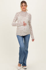 woman wearing a cream long sleeve maternity top with floral print and holding her baby bump, paired with blue flared jeans