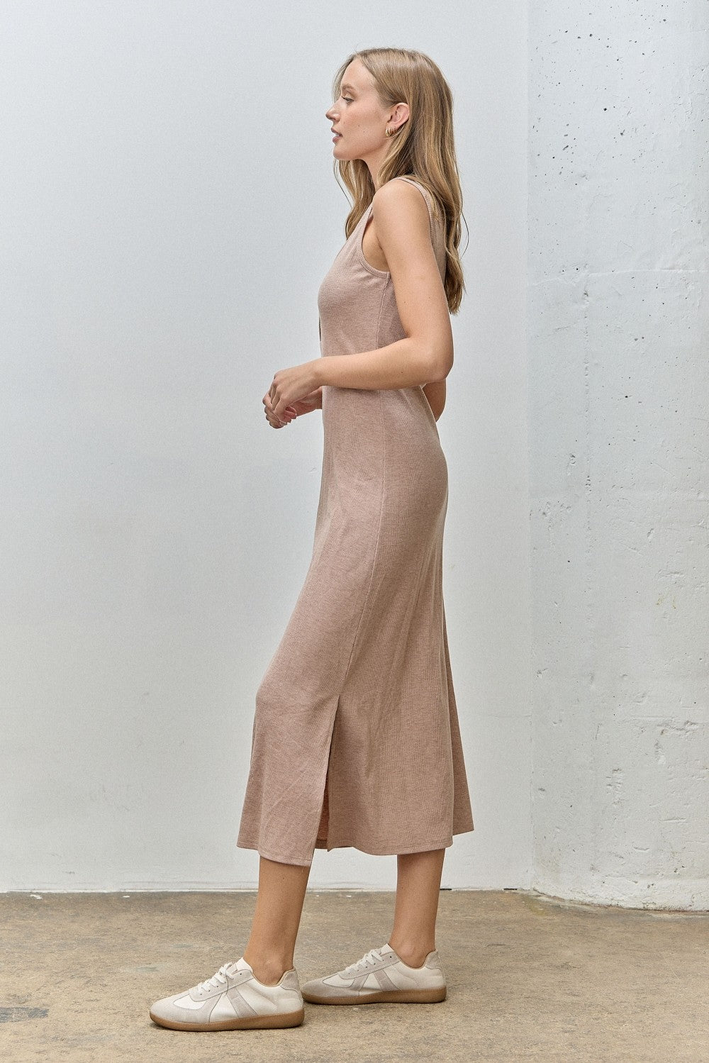 woman wearing a beige sleeveless maxi dress with a side slit and white sneakers