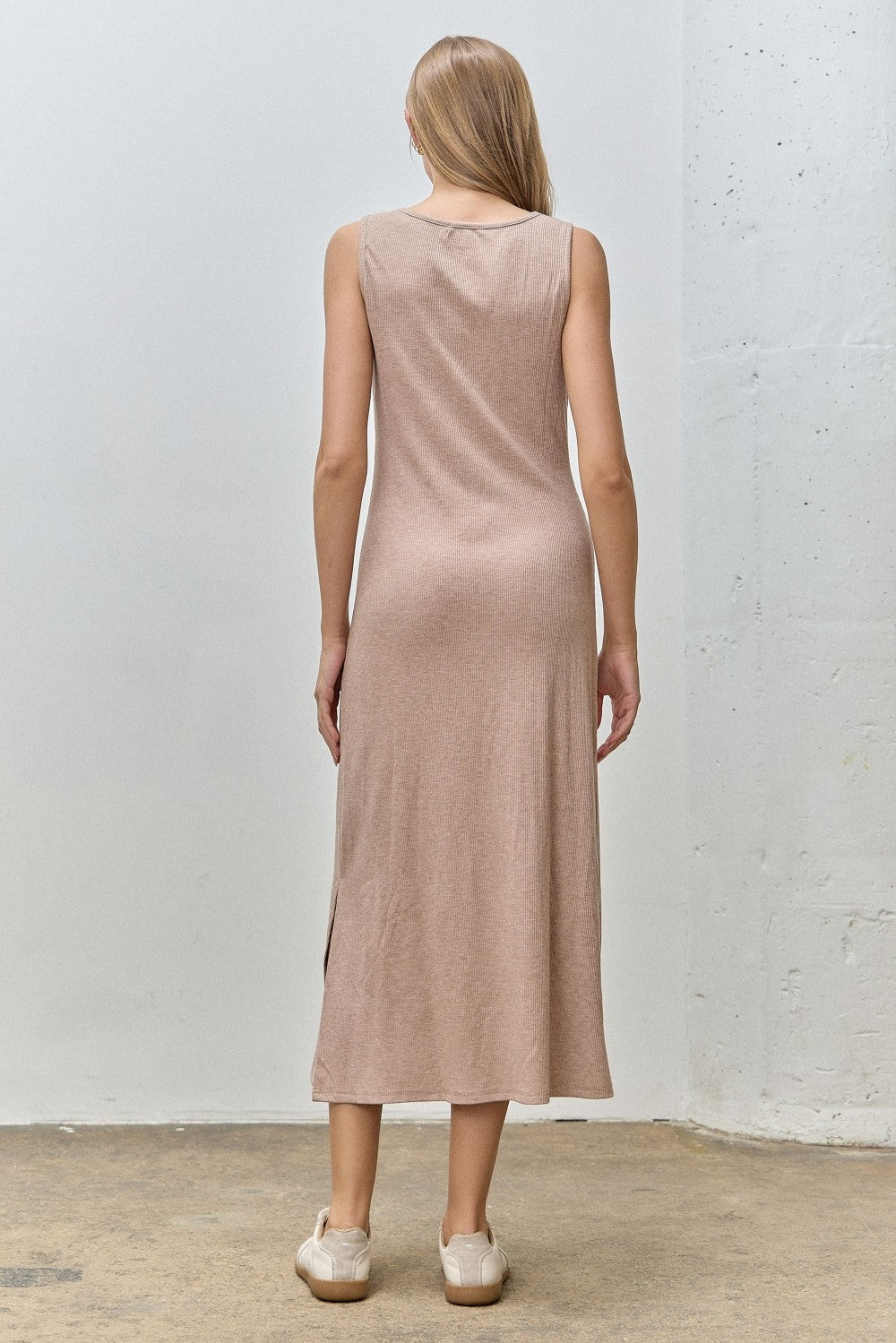 woman wearing a light brown sleeveless maxi dress with side slits, viewed from the back