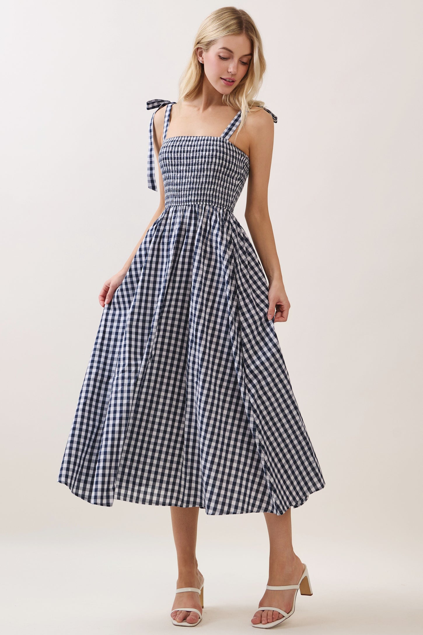 woman wearing a navy and white gingham midi dress with tie straps and a smocked bodice