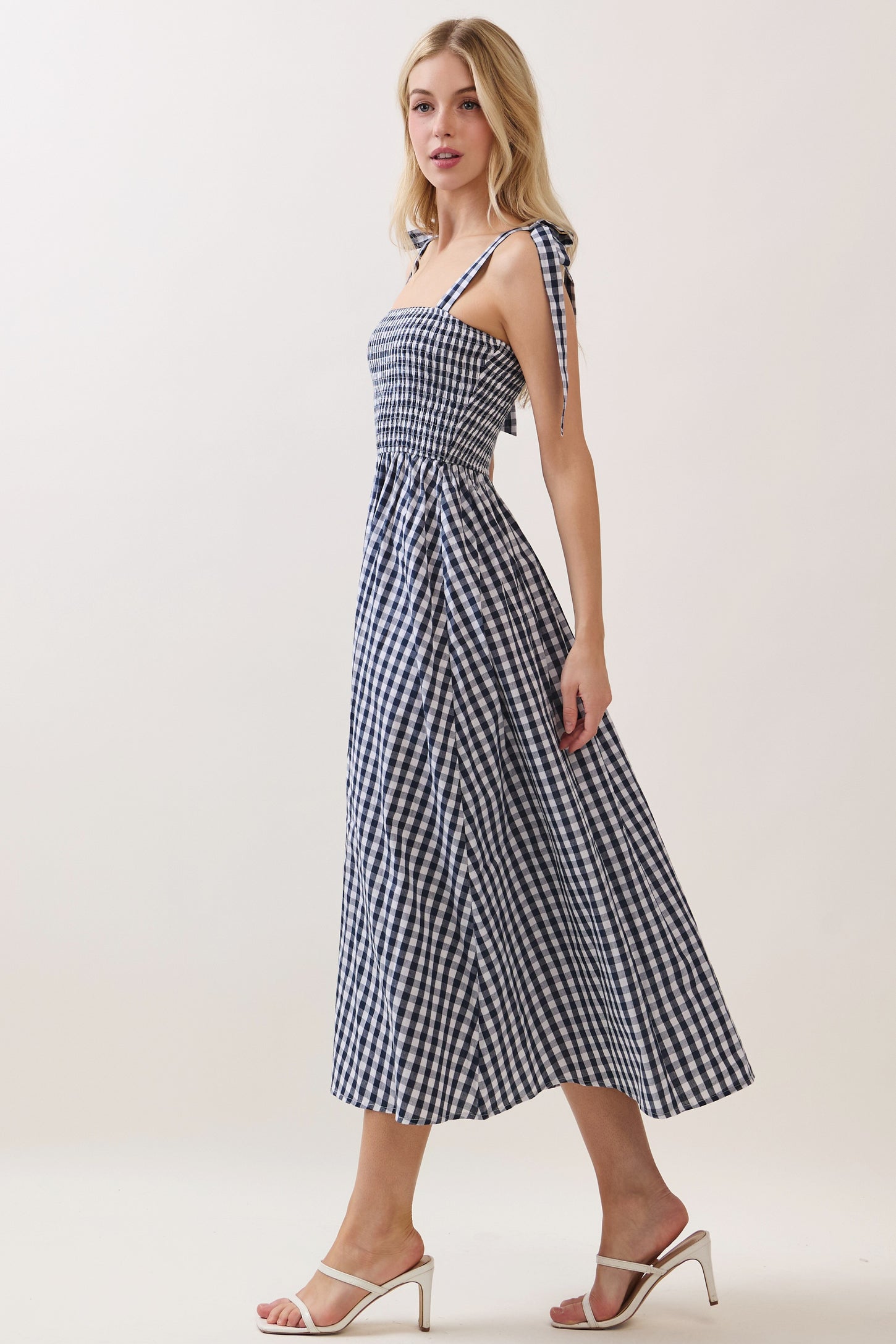 woman wearing a navy and white gingham midi dress with tie straps and a fitted bodice