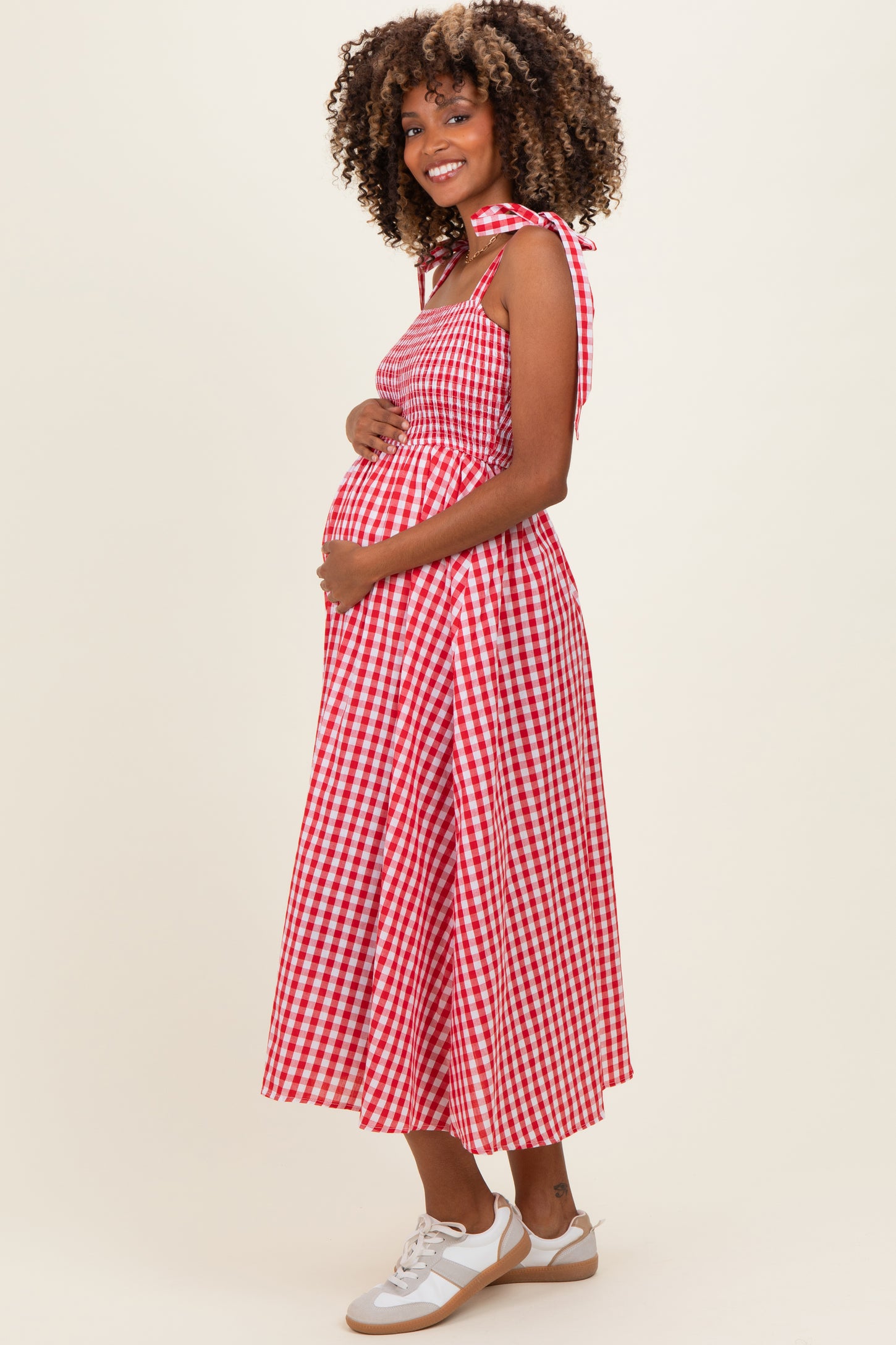 woman wearing a red and white gingham maternity dress with a tie shoulder and holding her baby bump