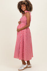 woman wearing a red and white gingham maternity dress with a tie shoulder and holding her baby bump