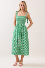 woman wearing a green gingham midi dress with tie straps and pockets, standing against a light background