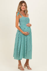 woman wearing a green and white gingham maternity dress with tie straps and a visible baby bump