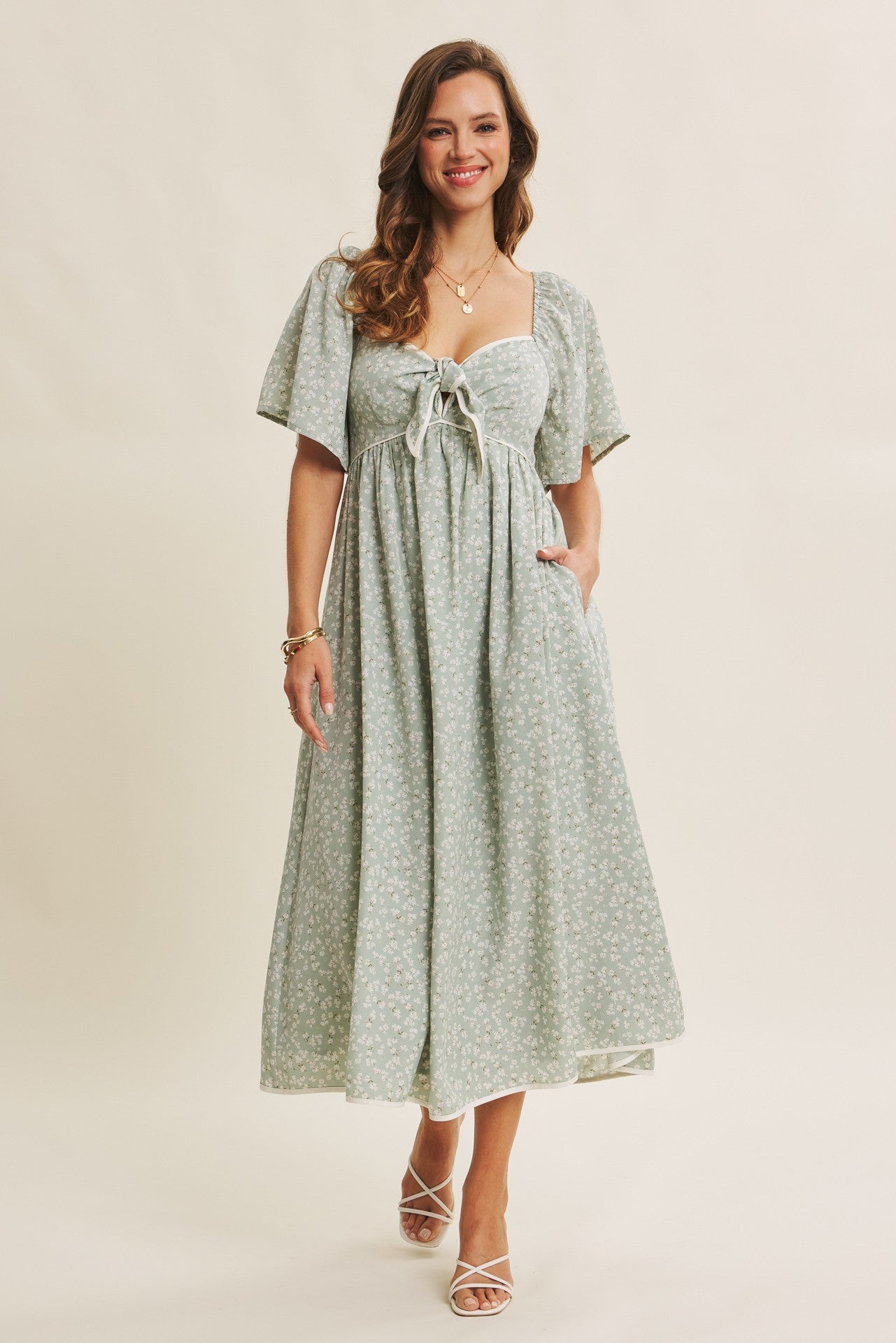 woman wearing a light green floral long dress with short puff sleeves and a tie-front detail