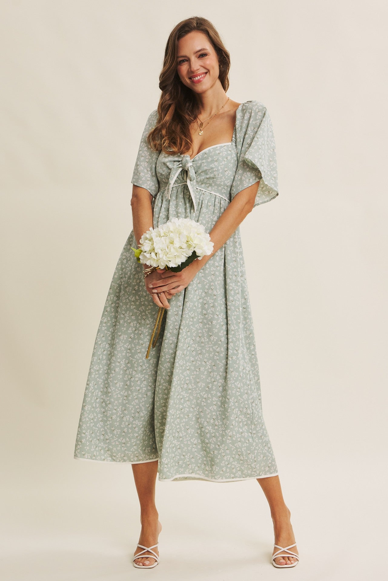 woman wearing a light green floral midi dress with a bow detail and puff sleeves, holding a bouquet of flowers