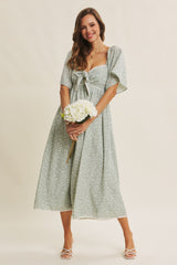 woman wearing a light green floral midi dress with a bow detail and puff sleeves, holding a bouquet of flowers