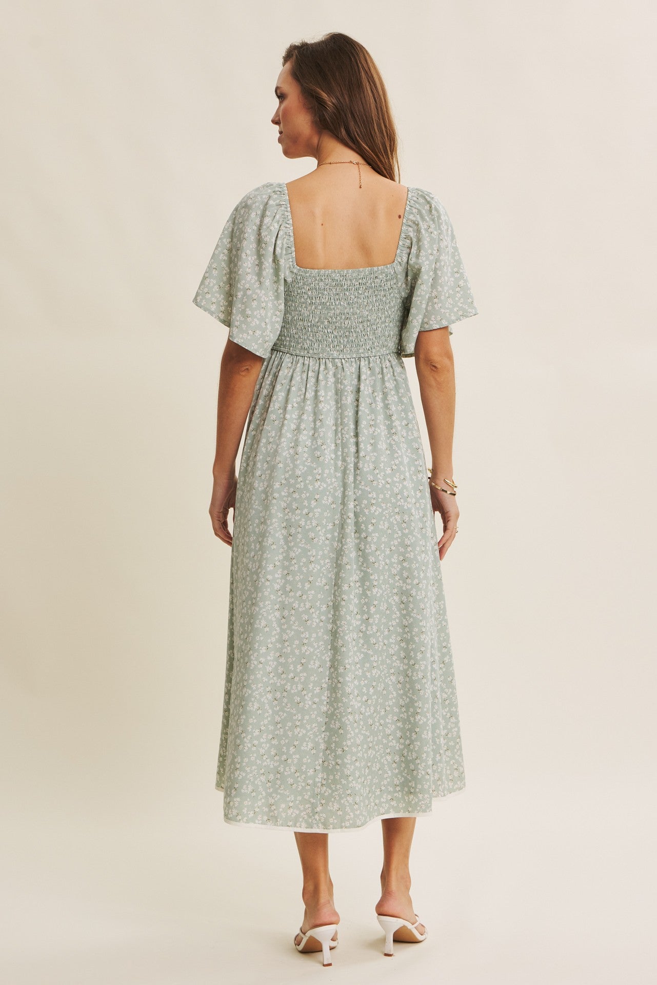 woman wearing a light green floral print midi dress with short puff sleeves and a smocked bodice, shown from the back