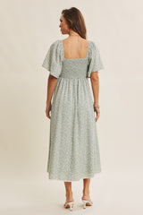 woman wearing a light green floral print midi dress with short puff sleeves and a smocked bodice, shown from the back