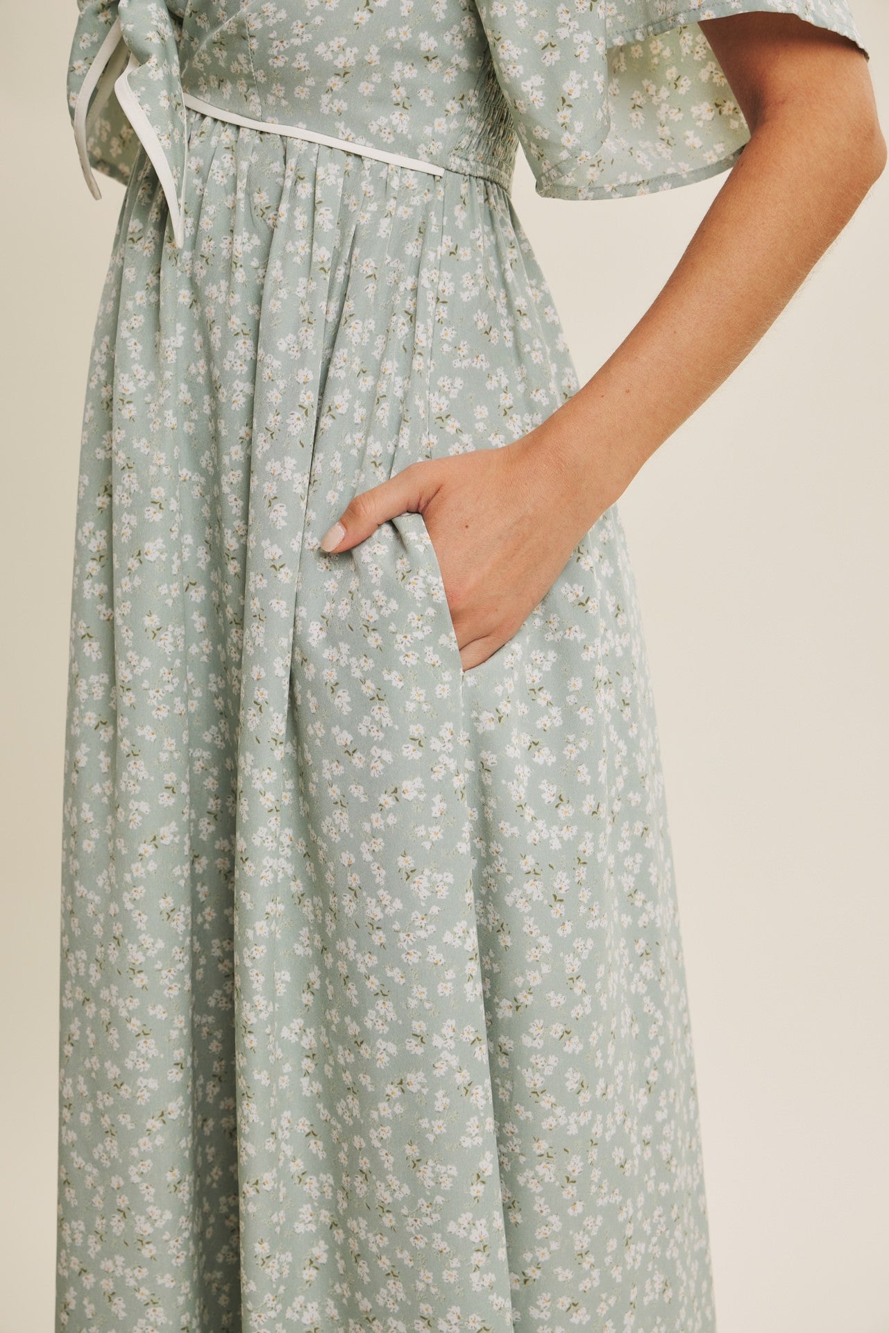 woman wearing a mint green floral maxi dress with a tie detail at the waist and hidden side pockets
