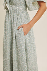 woman wearing a mint green floral maxi dress with a tie detail at the waist and hidden side pockets
