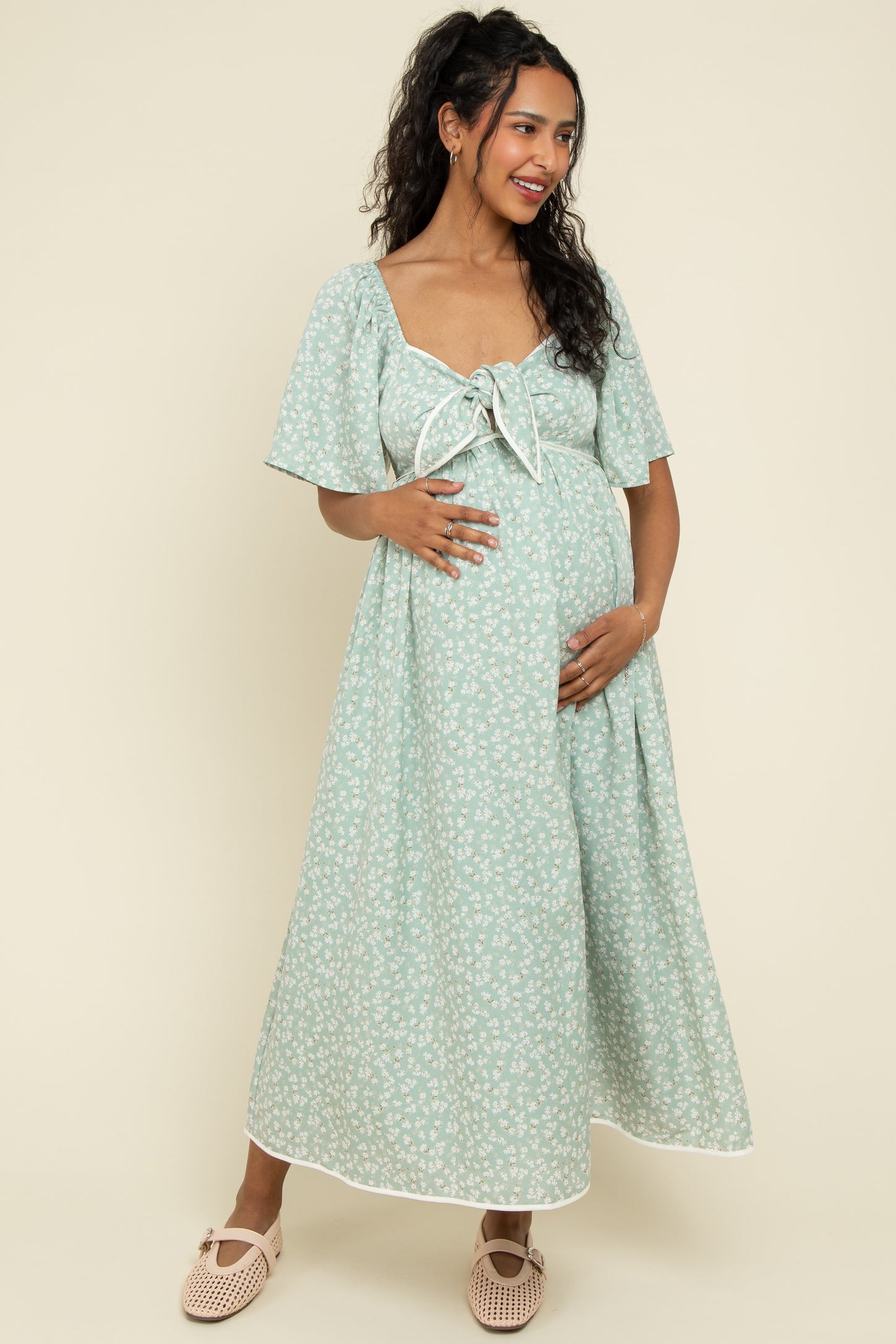 woman wearing a mint green floral maternity maxi dress with a tie front and short sleeves, holding her baby bump