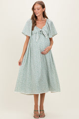 woman wearing a light green floral print maternity dress with a tie front, holding her baby bump