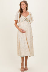 woman wearing a floral print maternity dress with a tie front, short flutter sleeves, and showing her baby bump