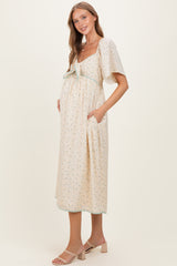 woman wearing a cream floral maternity dress with a front tie detail and short flutter sleeves, showing her baby bump