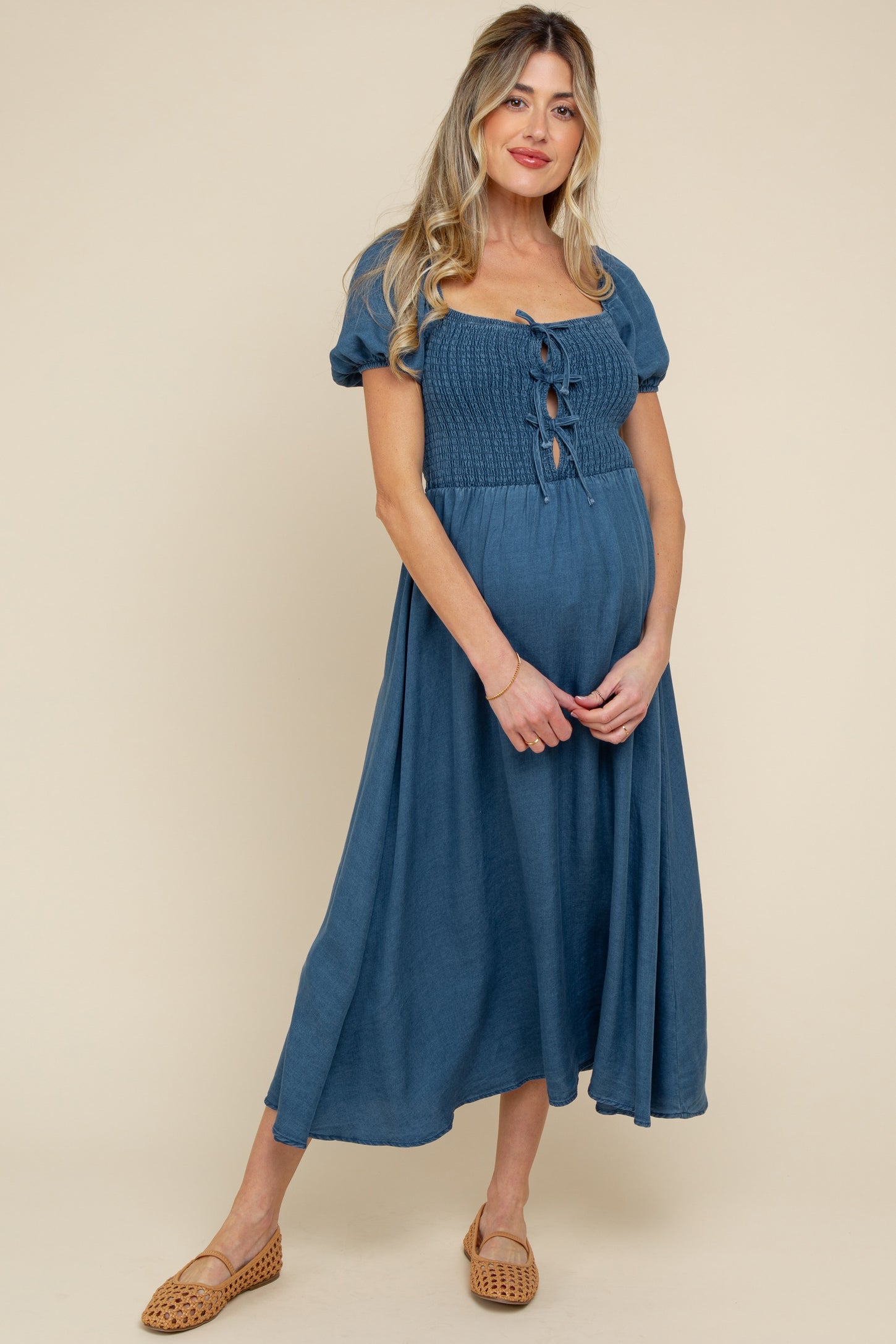 woman wearing a teal maternity dress with short puff sleeves and a front tie detail, showcasing her baby bump