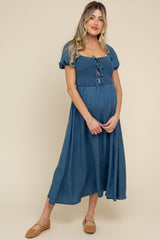 woman wearing a teal maternity dress with short puff sleeves and a front tie detail, showcasing her baby bump
