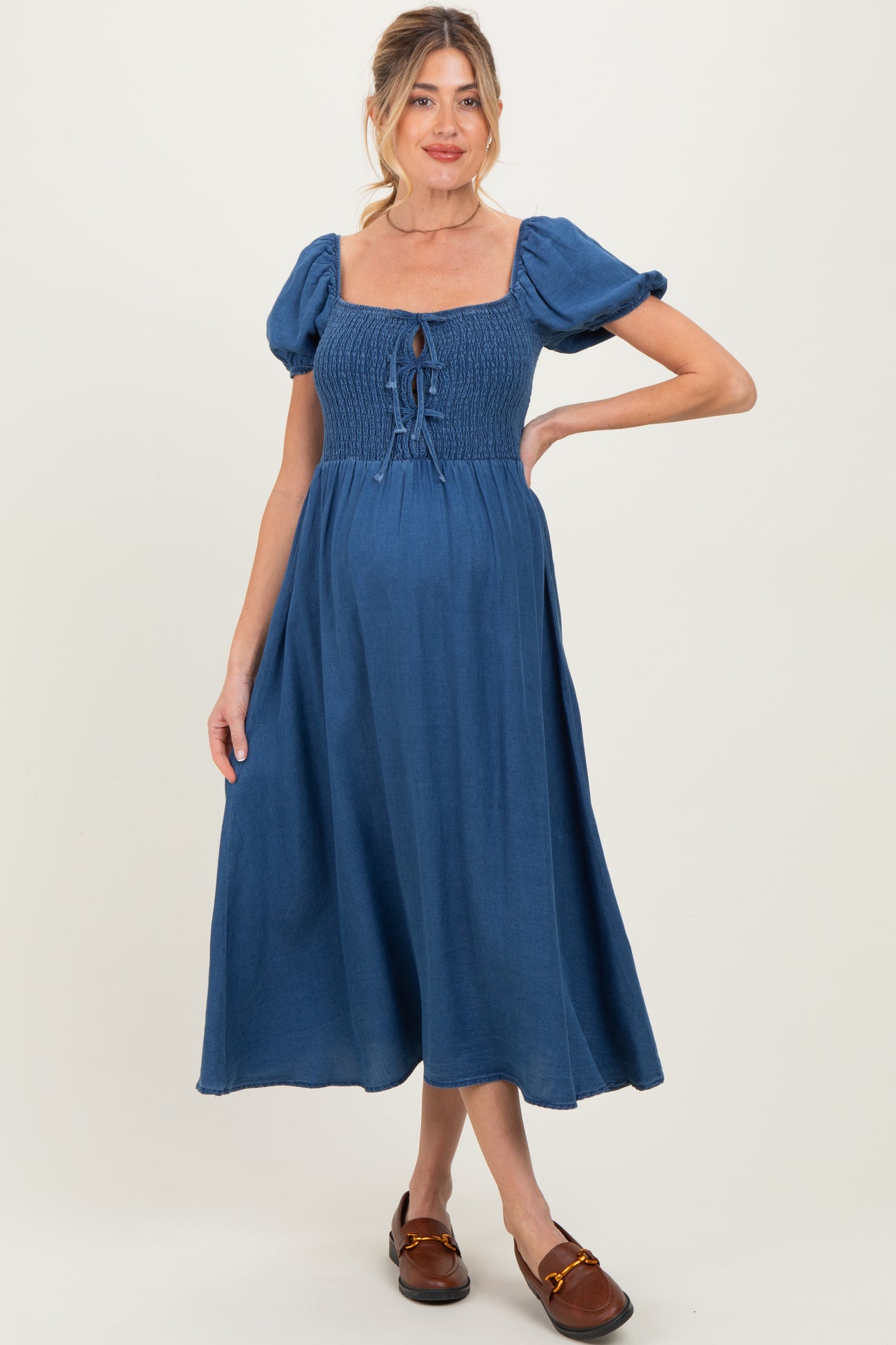 woman wearing a blue maternity dress with a smocked bodice, puff sleeves, and a flowing midi skirt