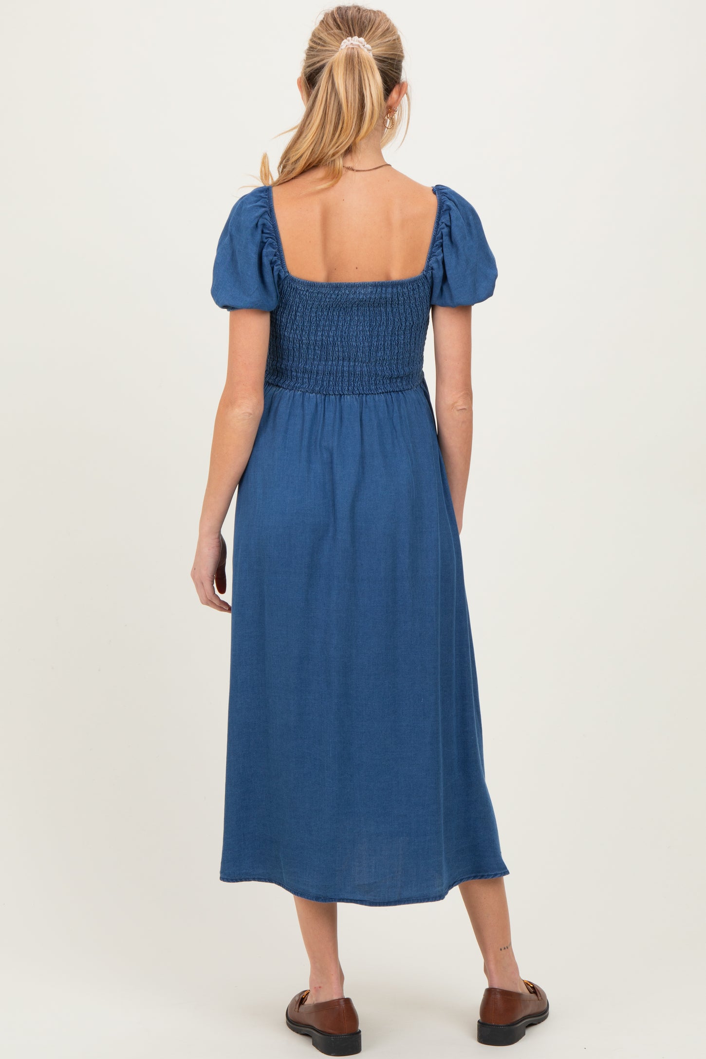 woman wearing a blue maternity dress with puff sleeves and a smocked bodice, showing the back view