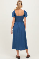 woman wearing a blue maternity dress with puff sleeves and a smocked bodice, showing the back view